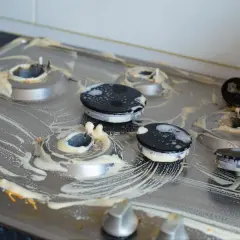 Brudna kuchenka gazowa z przypalonymi palnikami, pokryta pianą czyszczącą. Czym wyczyścić przypalone palniki kuchenki gazowej?