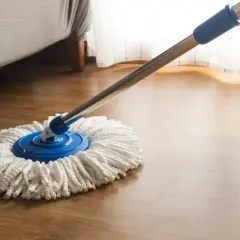Mop z białymi sznurkami na niebieskiej podstawie, gotowy do czyszczenia paneli. Obok stoi wiadro.