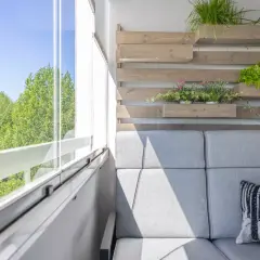 Nowoczesny balkon z szarą sofą i poduszką z lisem. Pionowe drewniane donice z ziołami i sałatą to świetne balkon inspiracje.