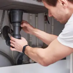 Mężczyzna montuje syfon pod zlewem. To kluczowy element instalacji hydraulicznej, który zapobiega wydostawaniu się nieprzyjemnych zapachów z kanalizacji.
