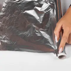 Dłonie próbują rozwinąć pogniecioną folię aluminiową, która wygląda, jakby laminator wciągnął folię.