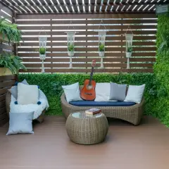 Przytulny balkon na parterze w bloku, z rattanowymi meblami, gitarą i mnóstwem zieleni. Idealne miejsce na relaks.