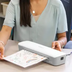 Kobieta laminuje rysunek dziecka. Zastanawiasz się laminator co to? To urządzenie, które zabezpiecza dokumenty.