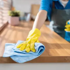 Ręka w żółtej rękawiczce czyści drewniany blat kuchenny, pokazując, czym wyczyścić blat kuchenny laminowany.