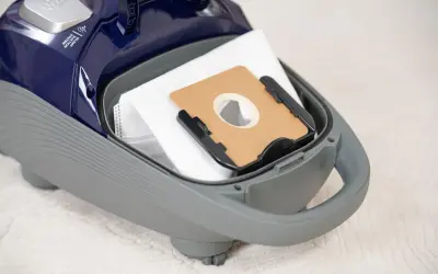 Worek do odkurzacza wewnątrz szarej obudowy. Na górze widoczny napis "Silent Suction System". Dowiedz się, ile decybeli ma odkurzacz.