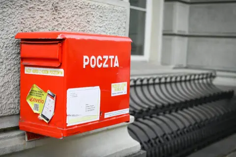 Czerwona skrzynka pocztowa z napisem "POCZTA" i naklejką o aplikacji Envelo. Jak wysłać list do Anglii? Wystarczy zaadresować kopertę i wrzucić do skrzynki.