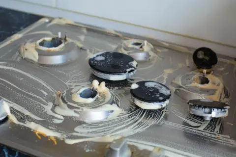 Brudna kuchenka gazowa z przypalonymi palnikami, pokryta pianą czyszczącą. Czym wyczyścić przypalone palniki kuchenki gazowej?