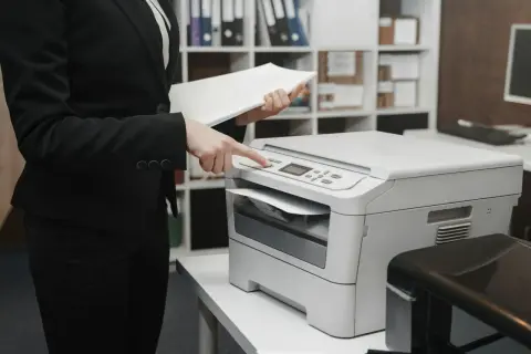 Kobieta w garniturze obsługuje drukarkę laserową czy atramentową, przygotowując dokumenty do druku.