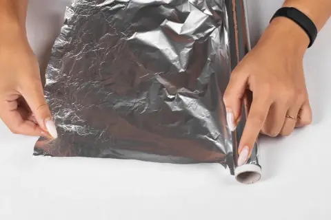 Dłonie próbują rozwinąć pogniecioną folię aluminiową, która wygląda, jakby laminator wciągnął folię.