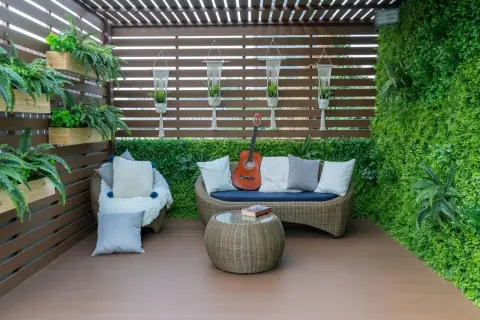 Przytulny balkon na parterze w bloku, z rattanowymi meblami, gitarą i mnóstwem zieleni. Idealne miejsce na relaks.