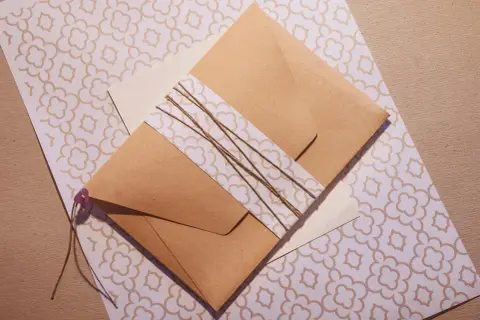 Jak zrobić kopertę? Brązowa koperta przewiązana sznurkiem, leży na papierze z delikatnym wzorem.
