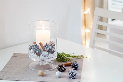 Prosty stroik świąteczny: świeca w szklanym wazonie z szyszkami, laskami cynamonu i orzechami.
