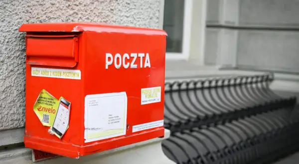 Czerwona skrzynka pocztowa z napisem "POCZTA" i naklejką o aplikacji Envelo. Jak wysłać list do Anglii? Wystarczy zaadresować kopertę i wrzucić do skrzynki.