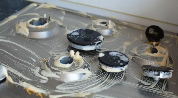 Brudna kuchenka gazowa z przypalonymi palnikami, pokryta pianą czyszczącą. Czym wyczyścić przypalone palniki kuchenki gazowej?