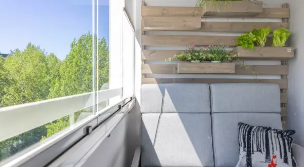 Nowoczesny balkon z szarą sofą i poduszką z lisem. Pionowe drewniane donice z ziołami i sałatą to świetne balkon inspiracje.