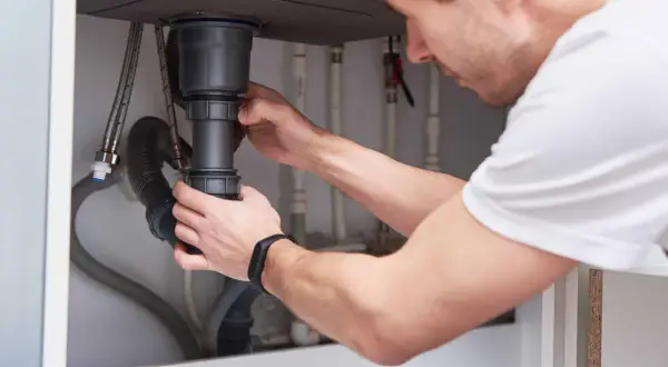 Mężczyzna montuje syfon pod zlewem. To kluczowy element instalacji hydraulicznej, który zapobiega wydostawaniu się nieprzyjemnych zapachów z kanalizacji.