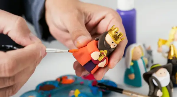 Tworzenie figurek do szopki z modeliny krok po kroku. Ręka maluje złotą koronę na głowie postaci.