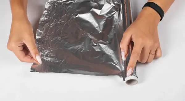 Dłonie próbują rozwinąć pogniecioną folię aluminiową, która wygląda, jakby laminator wciągnął folię.