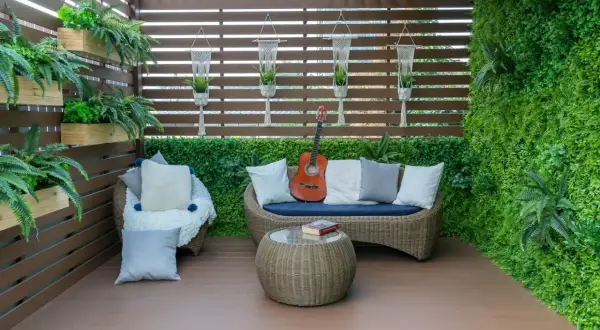 Przytulny balkon na parterze w bloku, z rattanowymi meblami, gitarą i mnóstwem zieleni. Idealne miejsce na relaks.