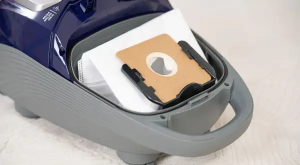 Worek do odkurzacza wewnątrz szarej obudowy. Na górze widoczny napis "Silent Suction System". Dowiedz się, ile decybeli ma odkurzacz.