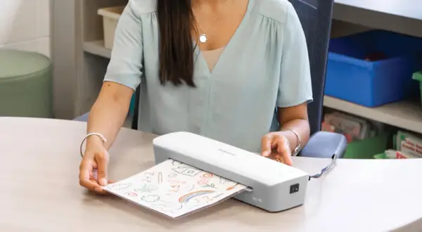 Kobieta laminuje rysunek dziecka. Zastanawiasz się laminator co to? To urządzenie, które zabezpiecza dokumenty.