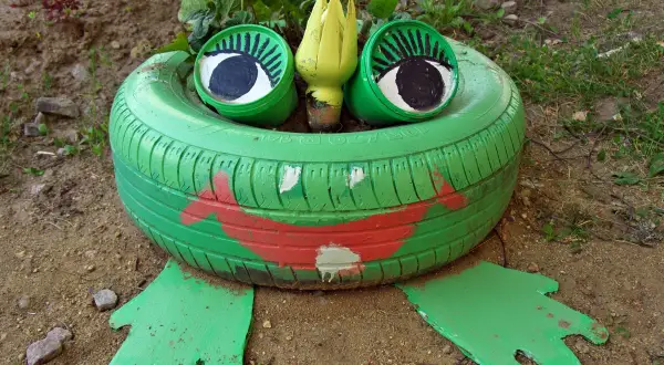 Zielona żaba z opony, z wielkimi oczami i czerwoną buzią, siedzi w ogrodzie. To urocze ozdoby z opony.
