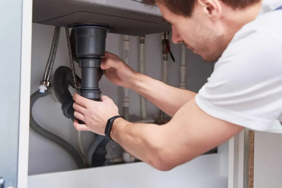 Mężczyzna montuje syfon pod zlewem. To kluczowy element instalacji hydraulicznej, który zapobiega wydostawaniu się nieprzyjemnych zapachów z kanalizacji.