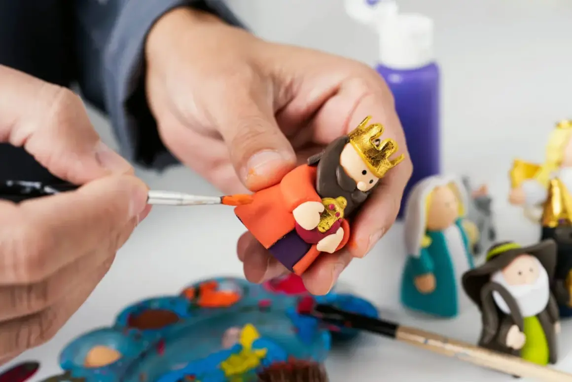 Tworzenie figurek do szopki z modeliny krok po kroku. Ręka maluje złotą koronę na głowie postaci.