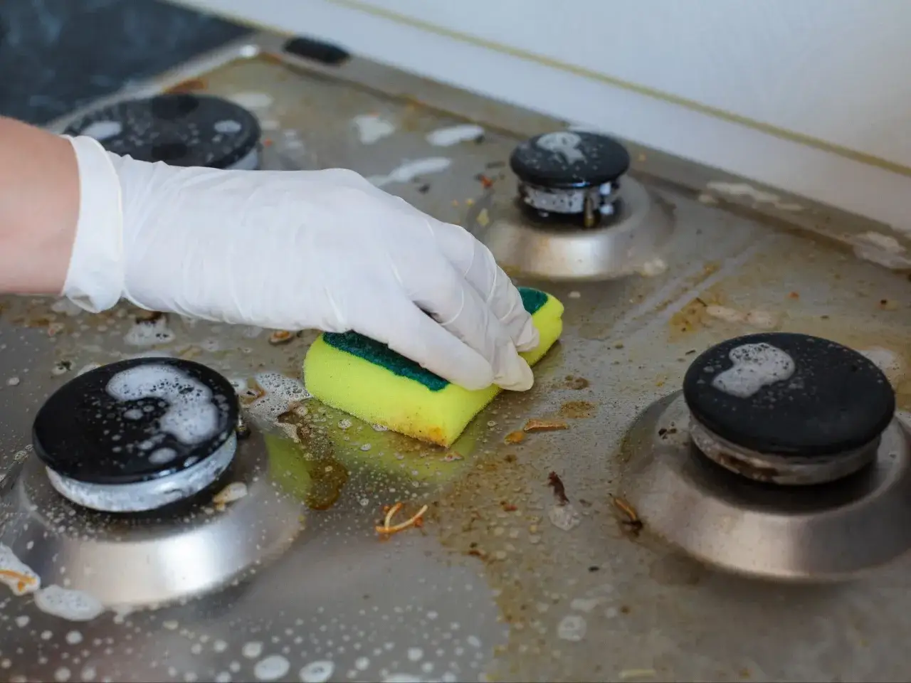 Rękawiczka i gąbka czyszczą przypalone palniki kuchenki gazowej. Dowiedz się, czym wyczyścić przypalone palniki kuchenki gazowej, by znów lśniły.