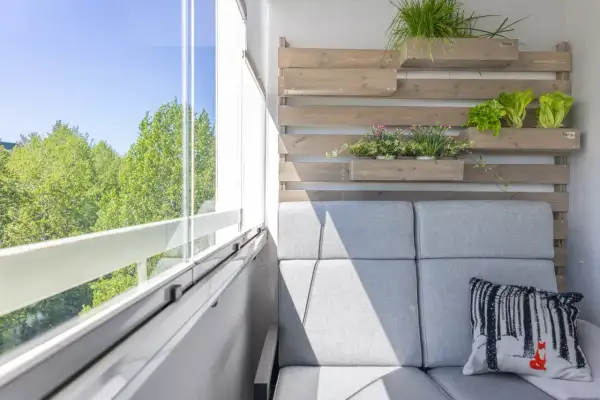 Nowoczesny balkon z szarą sofą i poduszką z lisem. Pionowe drewniane donice z ziołami i sałatą to świetne balkon inspiracje.