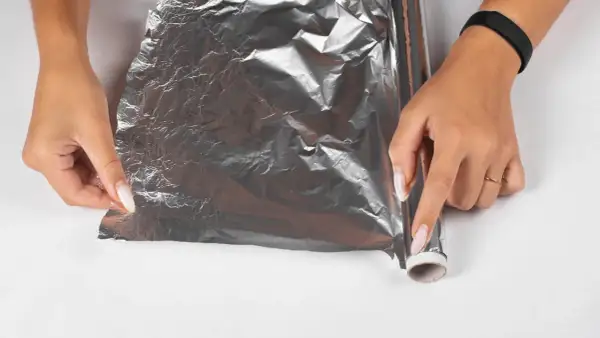 Dłonie próbują rozwinąć pogniecioną folię aluminiową, która wygląda, jakby laminator wciągnął folię.