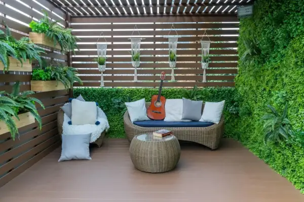 Przytulny balkon na parterze w bloku, z rattanowymi meblami, gitarą i mnóstwem zieleni. Idealne miejsce na relaks.