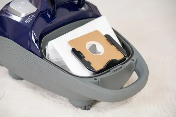 Worek do odkurzacza wewnątrz szarej obudowy. Na górze widoczny napis "Silent Suction System". Dowiedz się, ile decybeli ma odkurzacz.