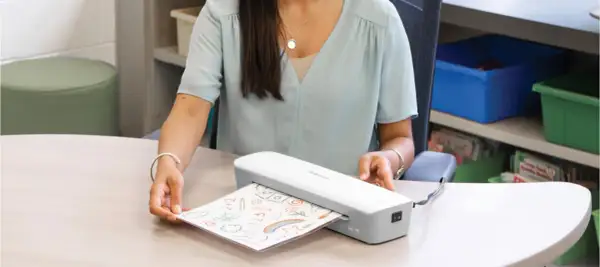 Kobieta laminuje rysunek dziecka. Zastanawiasz się laminator co to? To urządzenie, które zabezpiecza dokumenty.
